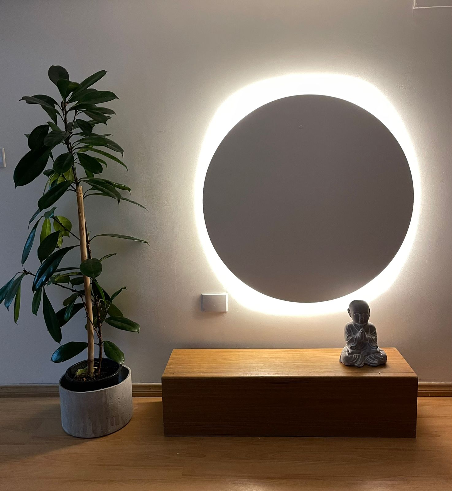 Ambiente do Satya Dojo com planta, banco de madeira, pequena figura sentada e iluminação circular na parede.
